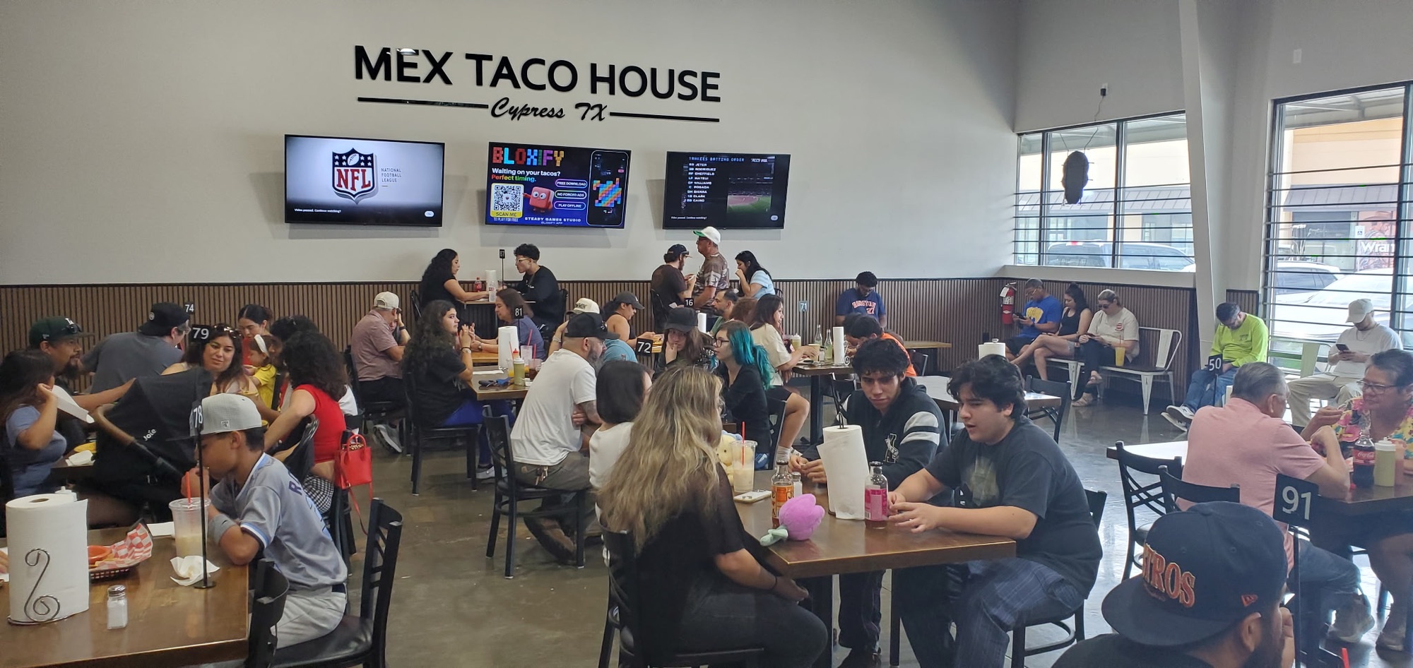 A full dining room at Mex Taco House in Cypress, with a Bloxify ad playing on the middle of three wall TVs